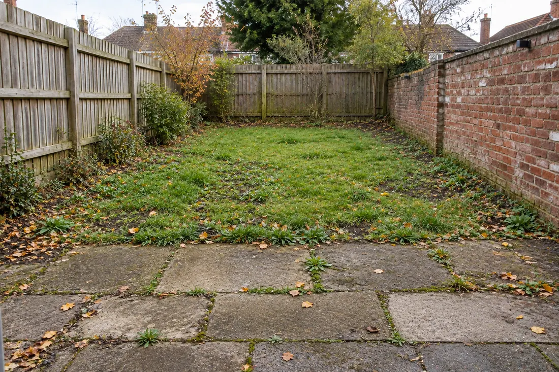 Worn rear garden with patchy lawn and broken slabs
